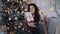 Portrait of a very pretty chalky young woman with a gift in her hand next to the Christmas tree.