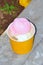 Portrait View Pink And White Vanilla-flavored Ice Cream In Orange Paper Tub Placed At The Garden Roadside