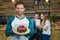Portrait of waiter holding plate of cake and customer in background