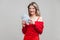 Portrait of wealthy beautiful young woman in red dress holding money, isolated on gray background