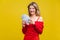 Portrait of wealthy beautiful young woman in red dress holding money, isolated on yellow background