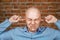 Portrait White bald man closes the ears in blue shirt on Brick wall background