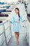 Portrait of white Caucasian brunette woman with tanned skin in blue dress by seashore lakeshore with yachts boats