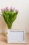 Portrait white picture frame mockup on wooden table. Modern vase with tulips.Scandinavian interior