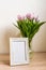 Portrait white picture frame mockup on wooden table. Modern vase with tulips.Scandinavian interior