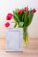 Portrait white picture frame mockup on wooden table. Modern vase with tulips.Scandinavian interior