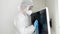 Portrait of woman afraid of viruses wearing protective medical suit and mask desinfecting TV with cleanser and detergent