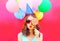 Portrait woman in a birthday cap is blowing lips is closes her eye with lollipop on stick over an air colorful balloons
