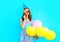 Portrait woman in a birthday cap holds an air colorful balloons is blowing lips is closes her eye with lollipop on stick