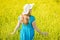 Portrait woman in blue dress and straw hat walk in yellow colza field