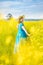 Portrait woman in blue dress and straw hat walk in yellow colza field
