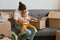 Portrait of woman with bun hairstyle wearing white t shirt sitting on sofa and holding her infant baby, unpacking boxes together