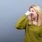 Portrait of woman covering nose with hand showing that something stinks against gray background