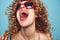 Portrait of a woman curly hair wide open mouth close-up studio sunglasses