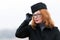 Portrait of woman in glasses and black coat. Concentrated red hair woman in hat. Portrait of business lady with red lips. Air-host