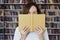 Portrait of woman in a library face half-covered by opened book, long hair. Young college student girl in co-working