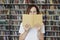 Portrait of woman in a library face half-covered by opened book, long hair. Young college student girl, concept of studying