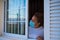 Portrait of woman looking outdoor from the window of her house in lockdown or quarantine to be safe from the coronavirus or covid-