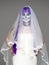 Portrait of woman looks at the camera with terrifying halloween skeleton makeup and purple wig bridal veil, wedding dress over gra