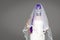 Portrait of woman looks at the camera with terrifying halloween skeleton makeup and purple wig bridal veil, wedding dress over gra
