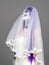 Portrait of woman looks upwards with terrifying halloween skeleton makeup and purple wig bridal veil, wedding dress over gray back