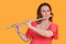 Portrait of a woman musician with a flute on a studio yellow background. Flutist with a large concert transverse flute in her