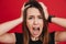 Portrait of woman in panic shouting and grabbing her head in fear or frustration, isolated over red background