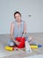 Portrait of a woman sitting on the floor of a room and stirring Wallpaper glue in a bucket. Concept of renovation in the