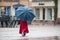 Portrait of woman walking with blue umbrella and red coat on cobbles place
