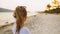 Portrait woman in a white tunic shirt on beach, near stormy sea. Girl in sunglasses. Female tourist walks. Rear view