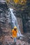 portrait of woman in yellow raincoat in front of autumn waterfall
