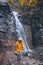 portrait of woman in yellow raincoat in front of autumn waterfall