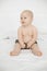 Portrait of wonderful smiling grey-eyed plump cherubic baby infant toddler wearing grey pants sitting on white bed.