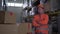 Portrait of worker with hands folded on chest stands in bright orange uniform near many boxes in warehouse