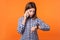 Portrait of worried young woman with brown hair wearing checkered shirt talking on phone. indoor studio shot isolated on orange