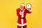 Portrait of yelling excited elderly man with gray beard wearing santa claus costume screaming in megaphone and showing wall clock