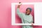 Portrait of young adorable girl holding big white polaroid frame picture of herself isolated on pink color background