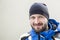 Portrait of young adult confident bearded man wearing warm sport clothes and hat at cold winter day. Smiling happy sportsman at st