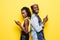 Portrait of a young afro american couple standing back to back using mobile phones isolated over yellow background