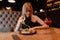 Portrait of young amazing woman sitting near black plate with salad and glass with red cocktail, eating in restaurant.