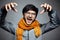 Portrait of young angry man making cat claws gesture, wearing glasses and orange scarf, background of gray.