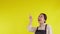 Portrait of young asian barista woman wearing apron presenting and thumbs up on yellow background.