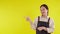 Portrait of young asian barista woman wearing apron presenting and thumbs up on yellow background.