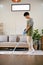 Portrait of young Asian man using stick vacuum cleaner to clean the carpet in living room