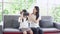 Portrait young Asian mother wearing virtual reality headset on amazed daughter while sits on couch in living room. New technology 