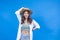 Portrait of young asian woman in casual clothing for vacation and beach vibe touching her straw hat isolated on blue background