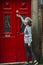 Portrait of a young Asian woman on a city street, knocking on the red doors of the house.