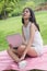 Portrait of young Asian woman sitting on green grass in park with legs crossed during summer day while using laptop computer.