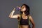 Portrait of young athletic and fit Asian Korean woman in fitness top holding bottle drinking water with skipping rope hanging on h