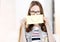 Portrait of young attractive businesswoman covering her mouth with yellow smiley paper in office